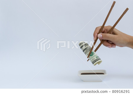 Dollars in a timber chopstick with soy sauce on a white with a copy space. Dollars in a timber chopstick with soy sauce on a white with a copy space. 80916291
