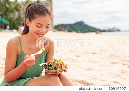 Woman eating poke bowl of ahi tuna on waikiki beach Hawaii. Local food fish salad vacation travel. Asian girl happy healthy eat Woman eating poke bowl of ahi tuna on waikiki beach Hawaii. Local food fish salad vacation travel. Asian girl happy healthy eat 80916297