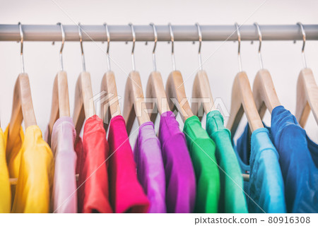 Clothes hanging on clothing rack wardrobe fashion apparel selection of rainbow color t-shirts on closet hangers. Womens wear in store shopping spring cleaning concept. Summer home wardrobe Clothes hanging on clothing rack wardrobe fashion apparel selection of rainbow color t-shirts on closet hangers. Womens wear in store shopping spring cleaning concept. Summer home wardrobe 80916308