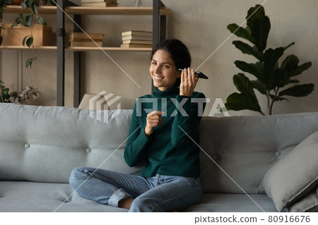 Smiling woman listening to voice message, holding phone near ear 80916676