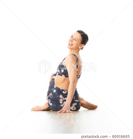 Rear view of young sporty female yoga instructor in bright white yoga studio, smiling cheerfully while looking in camera. Rear view of young sporty female yoga instructor in bright white yoga studio, smiling cheerfully while looking in camera. 80916685