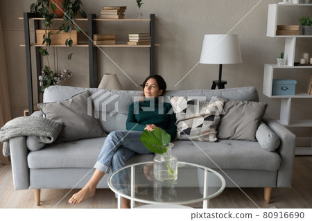 Satisfied woman relaxing on cozy couch in modern living room Satisfied woman relaxing on cozy couch in modern living room 80916690