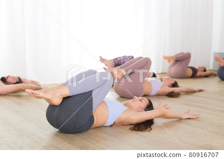 Group of young authentic sporty attractive people in yoga studio, practicing yoga lesson with instructor. Healthy active lifestyle, working out in gym Group of young authentic sporty attractive people in yoga studio, practicing yoga lesson with instructor. Healthy active lifestyle, working out in gym 80916707