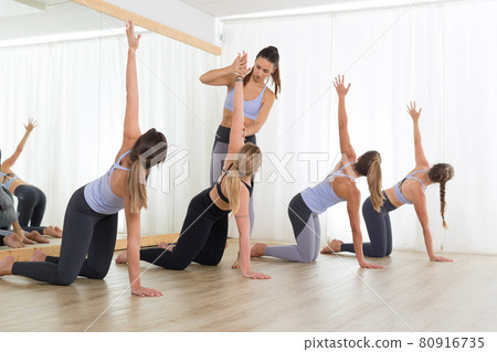 Group of young sporty sexy women in yoga studio, practicing yoga lesson with instructor. Healthy active lifestyle, working out indoors in gym 80916735
