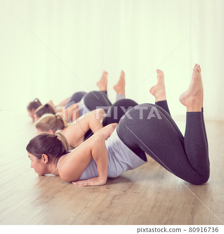 Group of young sporty sexy women in yoga studio, practicing yoga lesson with instructor, forming a line in Shishosana bent puppy dog asana pose. Healthy active lifestyle, working out indoors in gym 80916736