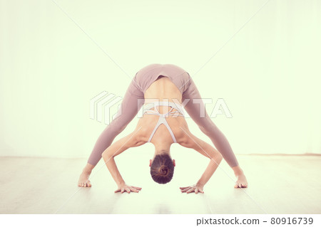 Portrait of gorgeous active sporty young woman practicing yoga in studio. Beautiful girl practice Dandayamana Bibhaktapada Paschimotthanasana, standing separate leg stretching pose 80916739