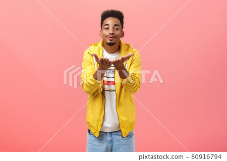 Blowing you sweet kisses. Cute and handsome stylish man with beard and afro hairstyle bending towards camera folding lips and smiling sending mwah with hands near breast over pink background Blowing you sweet kisses. Cute and handsome stylish man with beard and afro hairstyle bending towards camera folding lips and smiling sending mwah with hands near breast over pink background 80916794