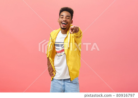 ha-ha loser. Portrait of happy amused energetic african american bearded male in yellow trendy jacket pointing at camera with index finger and laughing out loud humiliating mocking strange weirdo ha-ha loser. Portrait of happy amused energetic african american bearded male in yellow trendy jacket pointing at camera with index finger and laughing out loud humiliating mocking strange weirdo 80916797