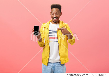 Man being amazed with cool new phone cannot hide happiness from device purchase holding smartphone pointing at gadget screen with excited and impressed face posing over pink background 80916816