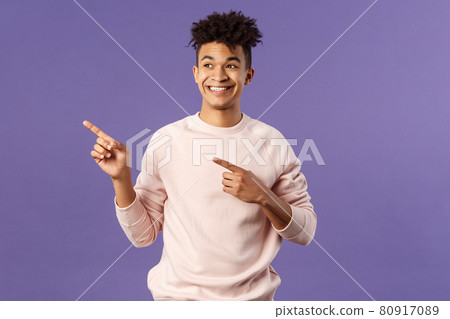 Portrait of enthusiastic, good-looking hispanic man with dreads, looking and pointing upper left corner with satisfied beaming smile, seeing cool thing, made his choice, purple background 80917089