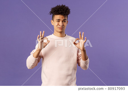 Portrait of skeptical young hispanic man rate something normal quality, show okay sign and grimacing judgemental, saying its not bad but average, standing purple background 80917093