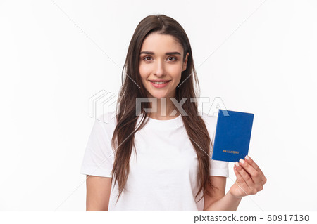 Travelling, holidays, summer concept. Close-up portrait of caucasian smiling happy woman in t-shirt, holding passport with and looking camera, buying flight ticket waiting for her plane in terminal Travelling, holidays, summer concept. Close-up portrait of caucasian smiling happy woman in t-shirt, holding passport with and looking camera, buying flight ticket waiting for her plane in terminal 80917130