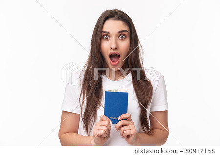 Travelling, holidays, summer concept. Close-up portrait of impressed, shocked young woman holding passport, drop jaw and staring astonished at camera, ready to travel, moving abroad 80917138