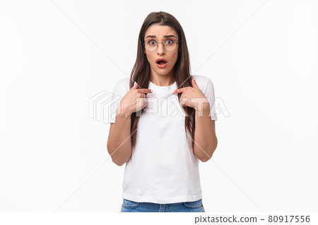 Waist-up portrait of nervous, surprised and silly young 20s woman in glasses, pointing at herself anxiously looking with opene mouth at camera, being worried as picked for mission 80917556