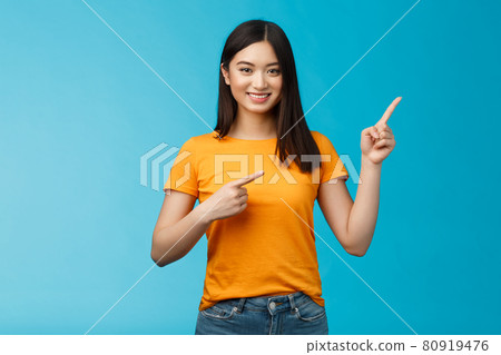 Friendly cheerful asian brunette girl inviting visit link interesting place, pointing upper right corner smiling joyfully camera, telling you about good promotion, stand blue background upbeat 80919476