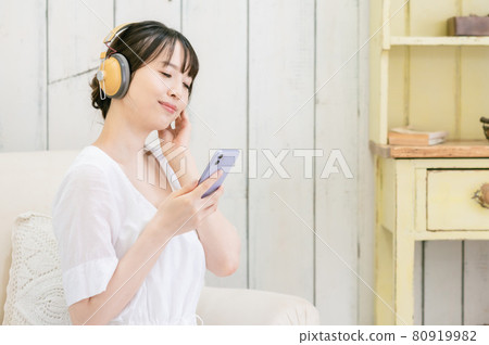 Young woman sitting on the sofa and listening to music through headphones Young woman sitting on the sofa and listening to music through headphones 80919982