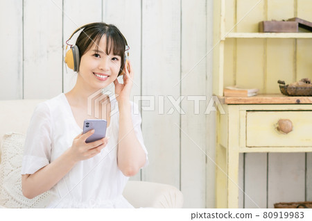 Young woman sitting on the sofa and listening to music through headphones 80919983