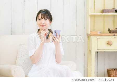 坐在沙發上，通過耳機聽音樂的年輕女人 80919985