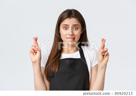 Employees, job employment, small business and coffee shop concept. Nervous cute cafe worker, saleswoman in black apron biting lip worried and cross fingers good luck, making wish, waiting for results 80920213