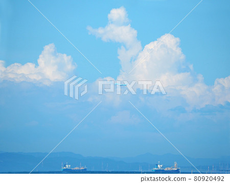 Uniquely shaped clouds and airplanes in the blue sky seen from the seaside 80920492