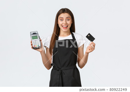 Grocery store employees, business and coffee shops concept. Excited smiling cafe worker, cashier in black apron showing how easy and safe purchase items contactless with credit card and POS terminal Grocery store employees, business and coffee shops concept. Excited smiling cafe worker, cashier in black apron showing how easy and safe purchase items contactless with credit card and POS terminal 80922249