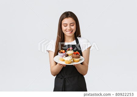 Grocery store employees, small business and coffee shops concept. Cheerful silly waitress want have bite of delicious cupcakes. Barista biting lip tempting to taste new desserts, white background Grocery store employees, small business and coffee shops concept. Cheerful silly waitress want have bite of delicious cupcakes. Barista biting lip tempting to taste new desserts, white background 80922253
