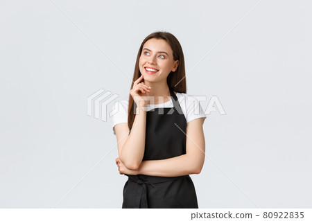 Small business, employees and coffee shop concept. Dreamy smiling beautiful saleswoman in black apron looking top right imaging. Store clerk or waiter standing in restaurant Small business, employees and coffee shop concept. Dreamy smiling beautiful saleswoman in black apron looking top right imaging. Store clerk or waiter standing in restaurant 80922835