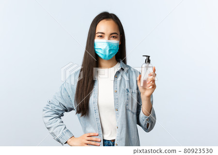 Social distancing lifestyle, covid-19 pandemic preventing virus concept. Young cute asian female in medical mask advice using hand sanitizer, showing soap bottle, explain measures during coronavirus 80923530