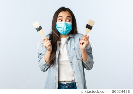 Social distancing lifestyle, covid-19 pandemic, self-isolation hobbies and leisure concept. Cheerful creative cute asian girl in medical mask eager to renovate house, holding two painting brushes Social distancing lifestyle, covid-19 pandemic, self-isolation hobbies and leisure concept. Cheerful creative cute asian girl in medical mask eager to renovate house, holding two painting brushes 80924458