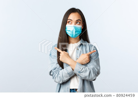 Social distancing lifestyle, covid-19 pandemic everyday life and leisure concept. Thoughtful indecisive asian girl making choice between two variants, pointing sideways and look left, wear mask Social distancing lifestyle, covid-19 pandemic everyday life and leisure concept. Thoughtful indecisive asian girl making choice between two variants, pointing sideways and look left, wear mask 80924459