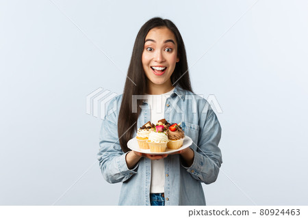Social distancing lifestyle, covid-19 pandemic, celebrating holidays during coronavirus concept. Excited asian girl holding plate with tasty cupcakes, smiling broadly, invite visit cafe with muffins Social distancing lifestyle, covid-19 pandemic, celebrating holidays during coronavirus concept. Excited asian girl holding plate with tasty cupcakes, smiling broadly, invite visit cafe with muffins 80924463