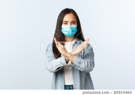 Social distancing lifestyle, covid-19 pandemic everyday life and leisure concept. Serious displeased asian girl in medical mask showing cross sign, disapprove or forbid something, tell to stop Social distancing lifestyle, covid-19 pandemic everyday life and leisure concept. Serious displeased asian girl in medical mask showing cross sign, disapprove or forbid something, tell to stop 80924464