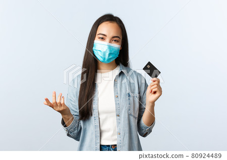 Social distancing lifestyle, covid-19 pandemic and contactless shopping concept. Carefree smiling asian girl in medical mask explain pros of credit card, paying for online order 80924489