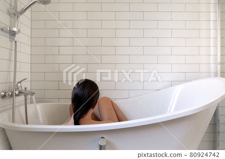Woman taking bath in bathtub in white bathroom 80924742