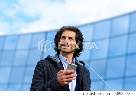 Modern confident young businessman in full suit standing outdoors with cityscape in the background Modern confident young businessman in full suit standing outdoors with cityscape in the background 80924786
