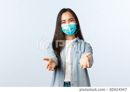 Social distancing lifestyle, covid-19 pandemic everyday life and leisure concept. Friendly lovely asian woman in medical mask reaching hands forward to take something or hold, white background 80924947