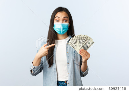 Social distancing lifestyle, covid-19 pandemic business and employement concept. Excited female asian employee suggest you earn lots money, pointing at cash dollars, wear medical mask Social distancing lifestyle, covid-19 pandemic business and employement concept. Excited female asian employee suggest you earn lots money, pointing at cash dollars, wear medical mask 80925436
