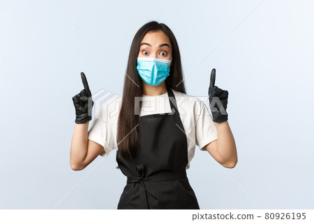 Covid-19 pandemic, social distancing, small business and preventing virus concept. Impressed asian female barista in medical mask and gloves pointing up, stare camera astonished Covid-19 pandemic, social distancing, small business and preventing virus concept. Impressed asian female barista in medical mask and gloves pointing up, stare camera astonished 80926195