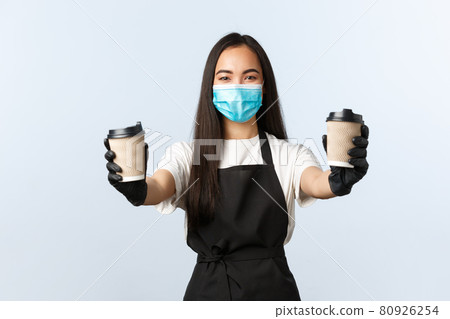 Covid-19, social distancing, small coffee shop business and preventing virus concept. Smiling friendly female barista, asian cafe owner in medical mask and gloves handing order, two cups of drinks Covid-19, social distancing, small coffee shop business and preventing virus concept. Smiling friendly female barista, asian cafe owner in medical mask and gloves handing order, two cups of drinks 80926254