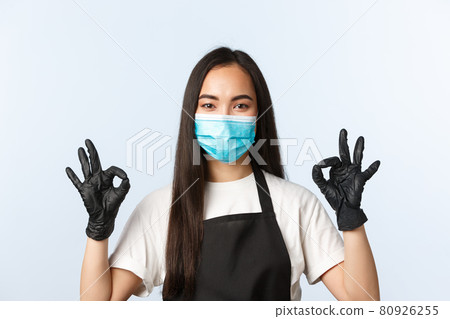 Covid-19 pandemic, coffee shop, small business and preventing virus concept. Smiling self-assured asian female cafe owner, employee in medical mask and gloves show okay 80926255