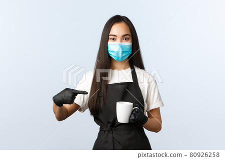 Covid-19, social distancing, small coffee shop business and preventing virus concept. Smiling asian barista in medical mask and gloves recommend try coffee at her cafe, pointing at cup Covid-19, social distancing, small coffee shop business and preventing virus concept. Smiling asian barista in medical mask and gloves recommend try coffee at her cafe, pointing at cup 80926258