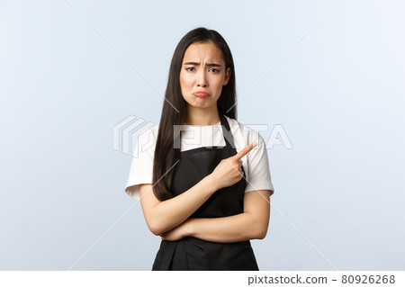 Coffee shop, small business and startup concept. Sad and gloomy disappointed female cafe owner, barista in black apron pointing finger right and sulking from despair or regret Coffee shop, small business and startup concept. Sad and gloomy disappointed female cafe owner, barista in black apron pointing finger right and sulking from despair or regret 80926268