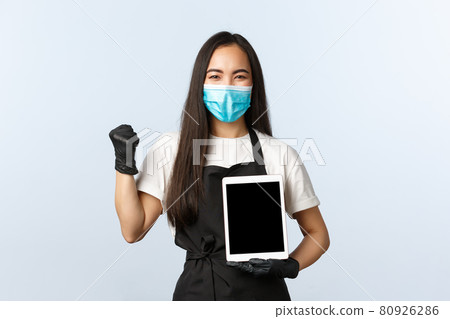 Covid-19, online orders, small coffee shop business and preventing virus concept. Satisfied happy asian female cafe owner fist pump, launch application, show digital tablet screen, wear medical mask Covid-19, online orders, small coffee shop business and preventing virus concept. Satisfied happy asian female cafe owner fist pump, launch application, show digital tablet screen, wear medical mask 80926286