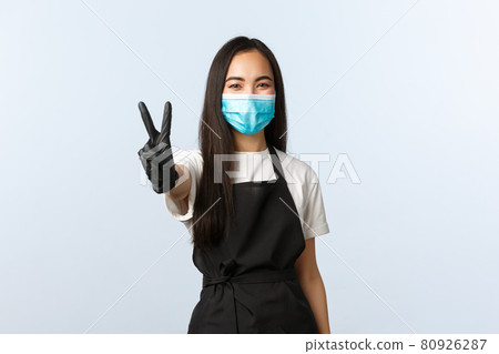 Covid-19, social distancing, small coffee shop business and preventing virus concept. Smiling cute asian female barista, restaurant or cafe worker in medical mask and gloves show v-sign, peace Covid-19, social distancing, small coffee shop business and preventing virus concept. Smiling cute asian female barista, restaurant or cafe worker in medical mask and gloves show v-sign, peace 80926287