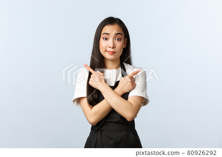 Coffee shop, small business and startup concept. Cute cafe employee in black apron asking advice as pointing sideways. Pretty asian waitress or barista showing left and right choices being indecisive Coffee shop, small business and startup concept. Cute cafe employee in black apron asking advice as pointing sideways. Pretty asian waitress or barista showing left and right choices being indecisive 80926292