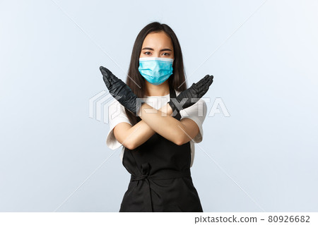 Covid-19, social distancing, small coffee shop business and preventing virus concept. Serious young barista, asian cafe staff forbid customers come inside without medical mask, show cross stop sign 80926682