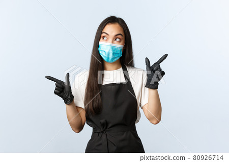 Covid-19, social distancing, small coffee shop business and preventing virus concept. Thoughtful asian barista, cafe owner in medical mask and gloves making choice, pointing sideways Covid-19, social distancing, small coffee shop business and preventing virus concept. Thoughtful asian barista, cafe owner in medical mask and gloves making choice, pointing sideways 80926714