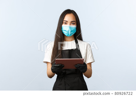 Covid-19, online orders, small coffee shop business and preventing virus concept. Friendly-looking asian female barista ready take your order, wear medical mask and gloves, hold digital tablet Covid-19, online orders, small coffee shop business and preventing virus concept. Friendly-looking asian female barista ready take your order, wear medical mask and gloves, hold digital tablet 80926722