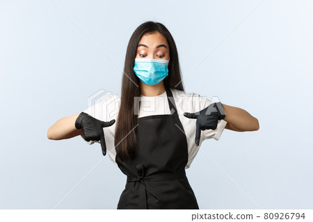 Covid-19 pandemic, social distancing, small business and preventing virus concept. Intrigued and curious asian coffee shop barista, employee in medical mask and gloves peeking down, pointing bottom Covid-19 pandemic, social distancing, small business and preventing virus concept. Intrigued and curious asian coffee shop barista, employee in medical mask and gloves peeking down, pointing bottom 80926794