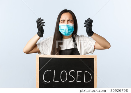 Small business, covid-19 pandemic, preventing virus and employees concept. Distressed and alarmed asian female coffee shop staff, cafe owner in medical mask cant work on lockdown, closed sign Small business, covid-19 pandemic, preventing virus and employees concept. Distressed and alarmed asian female coffee shop staff, cafe owner in medical mask cant work on lockdown, closed sign 80926798